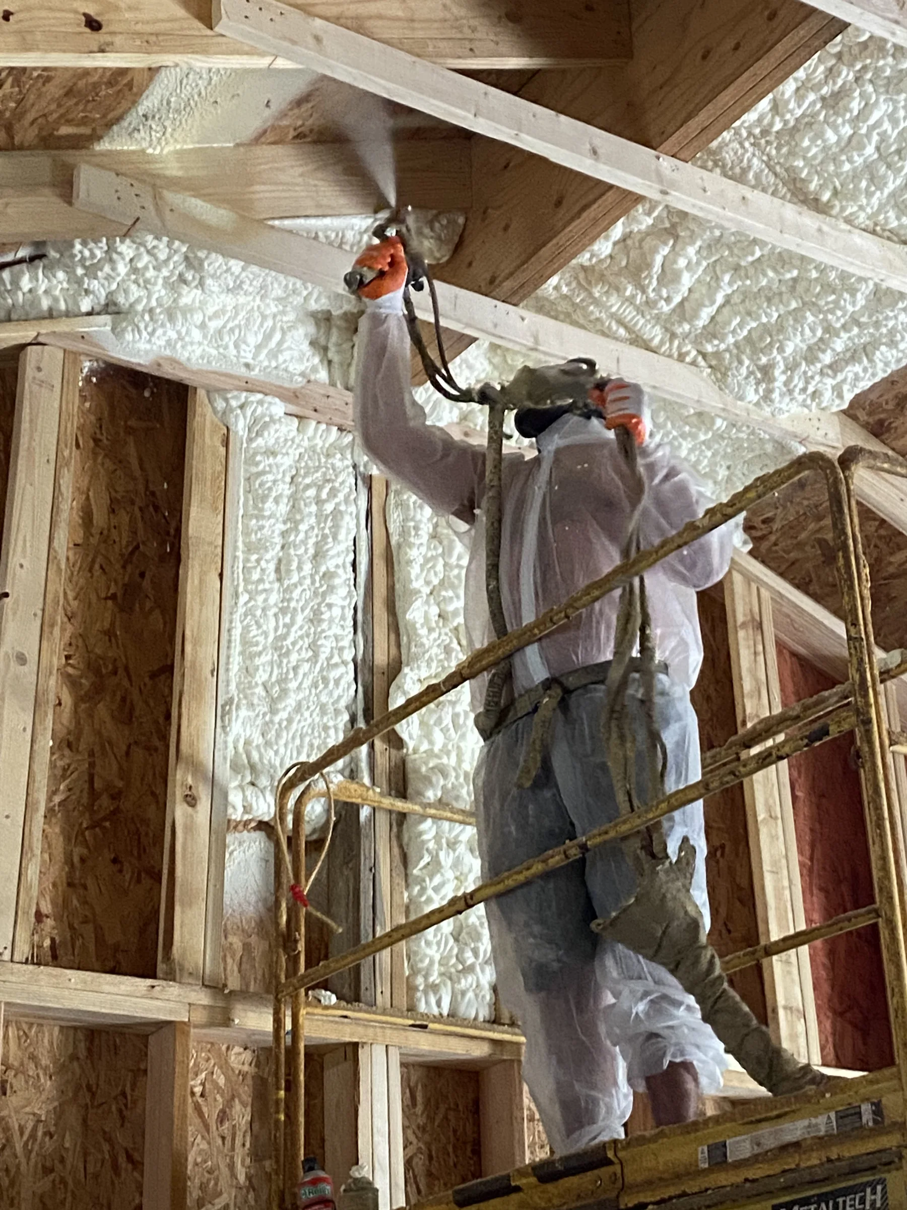 Spray foam installer applying open-cell foam to a roofline